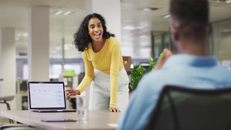 video of happy biracial businesswoman using laptop and talking with male colleague
