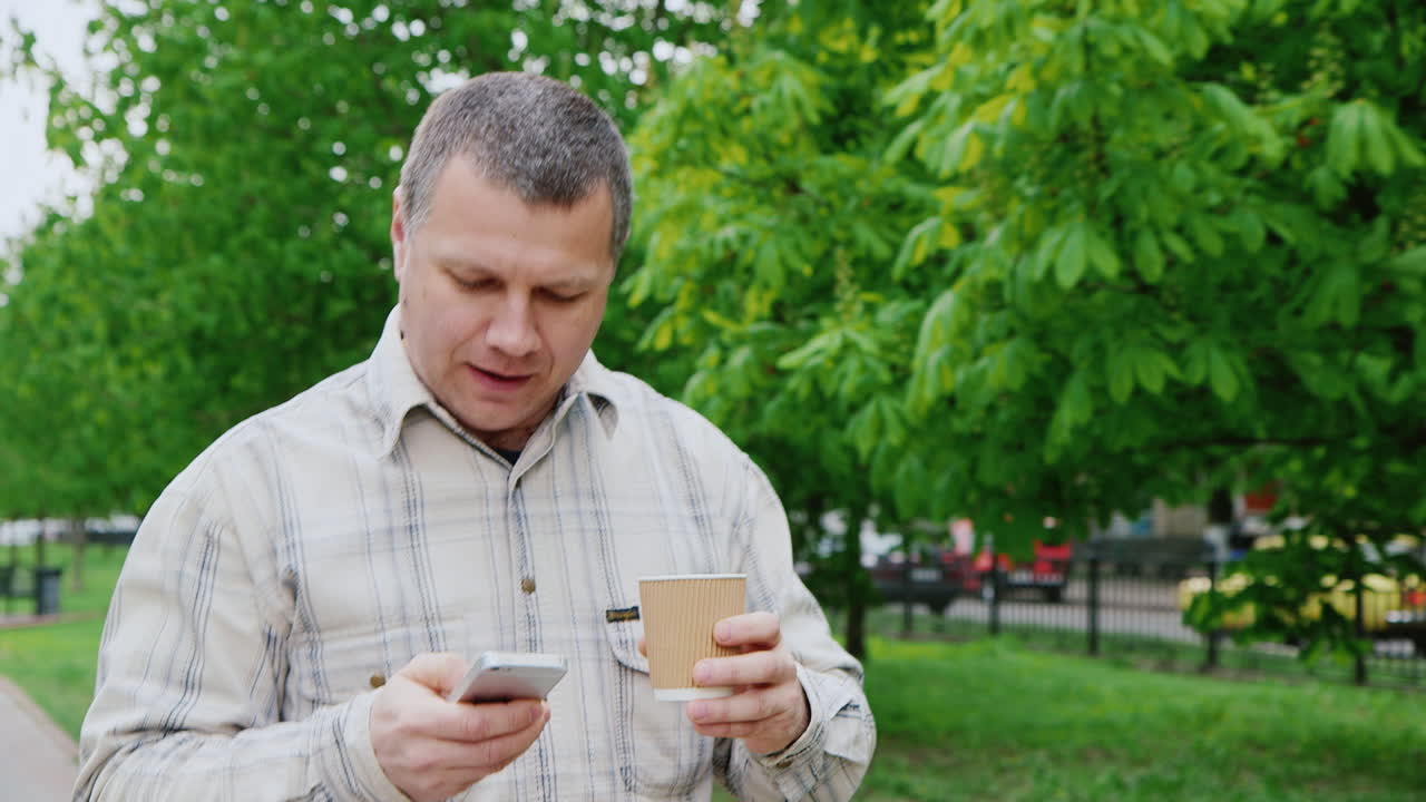 hombre de mediana edad tomando café mientras camina por el parque de la ciudad
