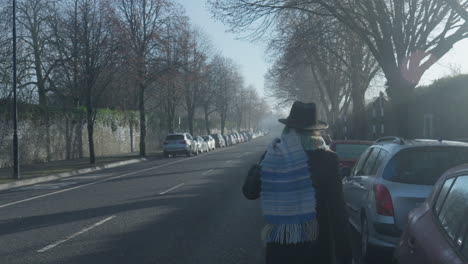 Woman-throws-on-scarf-walking-on-road-in-misty-sunny-morning