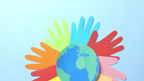 close-up van handen samen met een globe gemaakt van kleurrijk papier op blauwe achtergrond met kopieerruimte