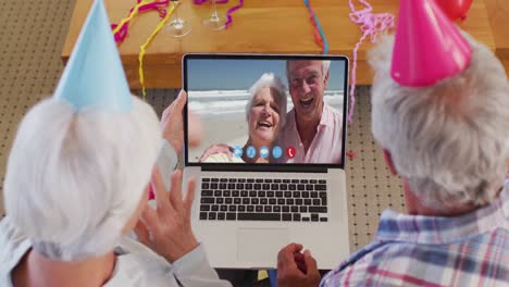 Pareja-Mayor-Caucásica-En-Video-Chat-Portátil-Usando-Sombreros-De-Fiesta-En-Casa