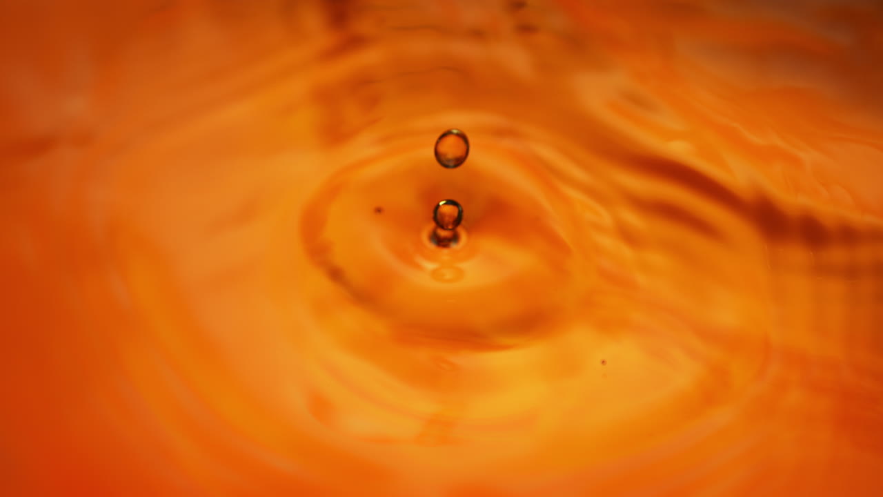 위스키 방울이 황금색 액체의 파란색 표면에 흘러내려 매크로와 느린 동작으로 스플래시 크로너를 만니다.