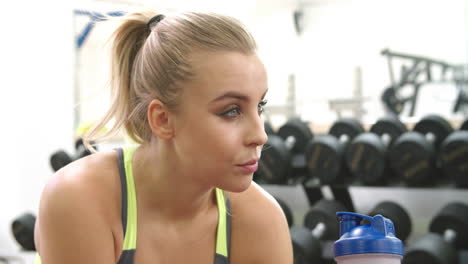 joven mujer caucásica bebiendo un batido de proteínas en un gimnasio