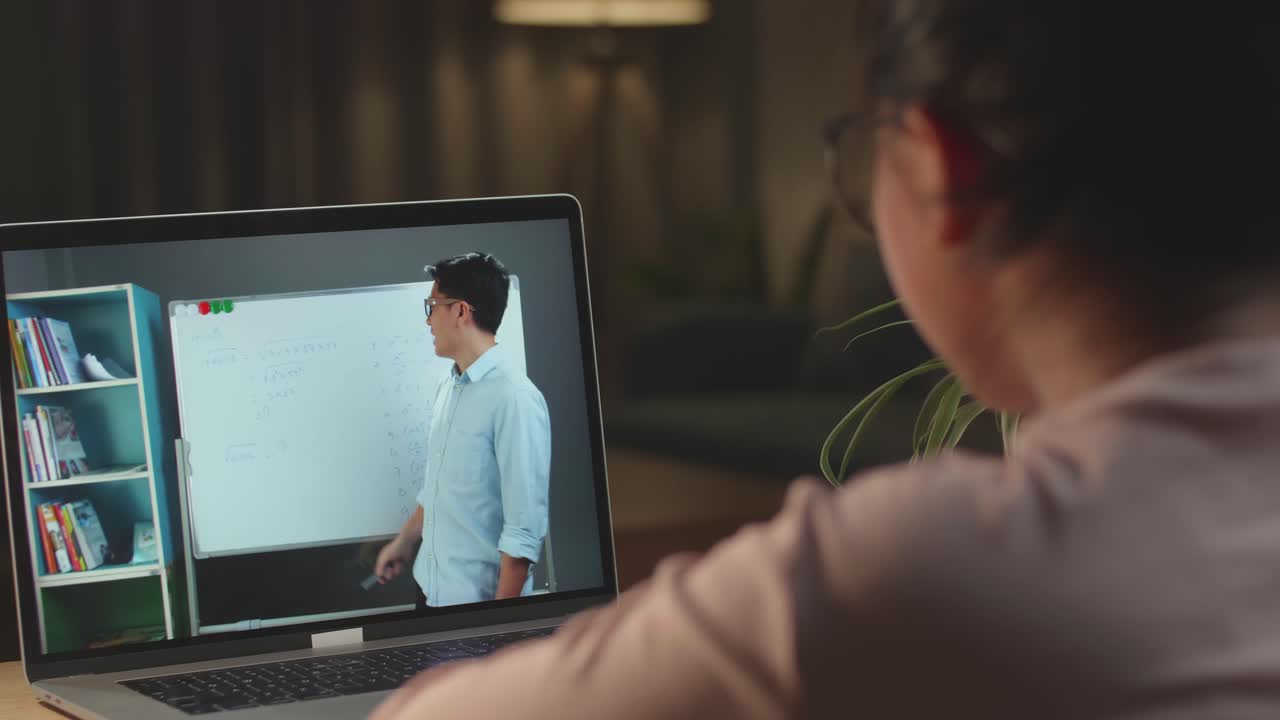 School Teen Girl Student Distance Learning With Online Teacher On Computer Screen. Web Tutor Gives Remote Class Teaching Teenage Pupil Elearning From Home At Night. Over Shoulder Close Up View