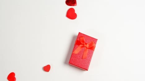 Red-gift-box-and-red-hearts-on-white-surface-4k