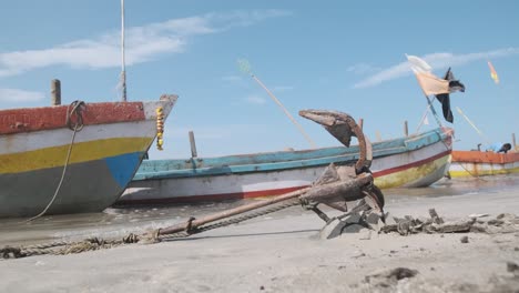 rusty anchor in the sand shore holding small colourful indian fishing boats in place