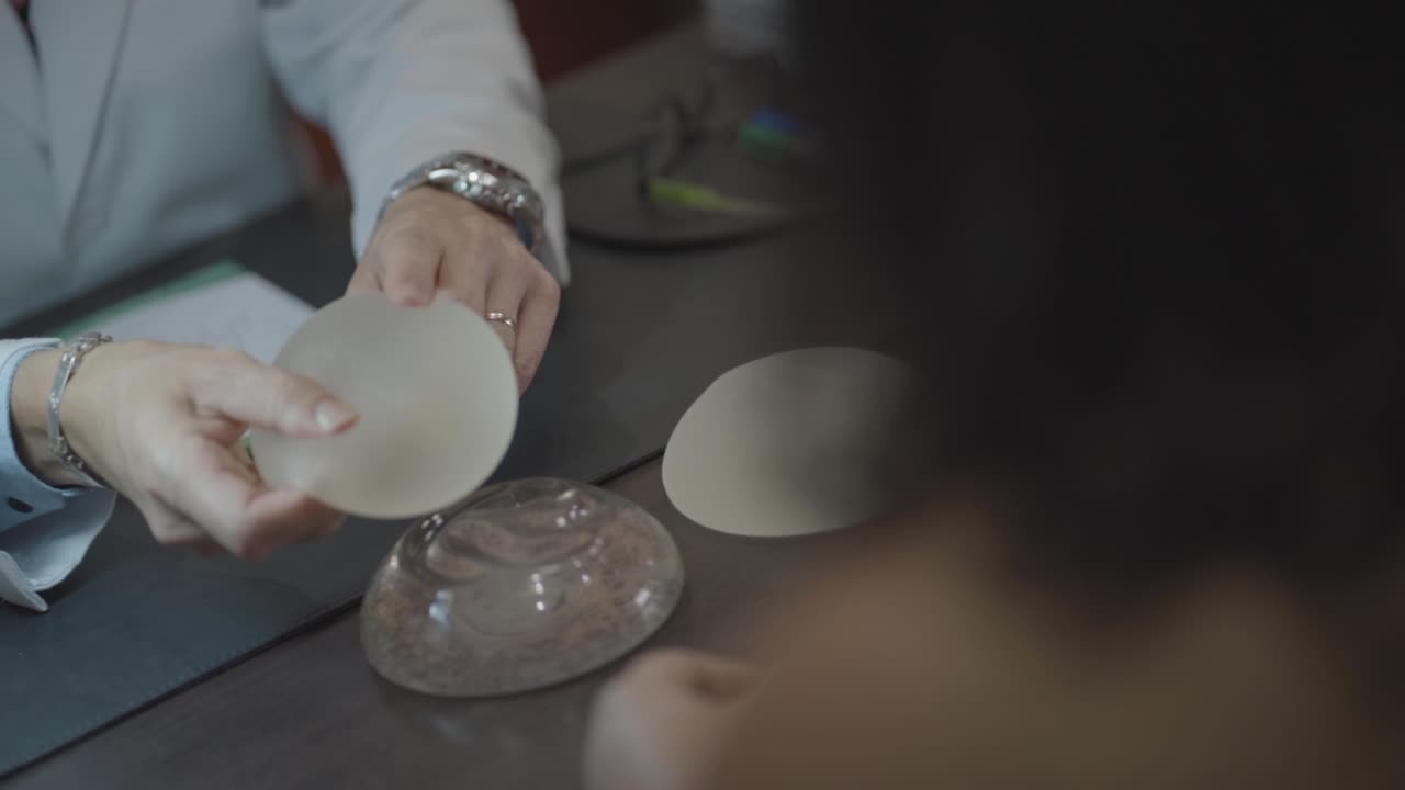 médico en cámara lenta y paciente tocando la prótesis de mama de silicona de cerca, metiendo con el dedo