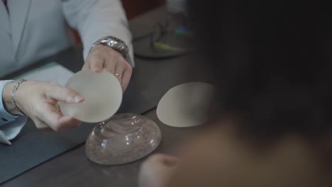 médico en cámara lenta y paciente tocando la prótesis de mama de silicona de cerca, metiendo con el dedo