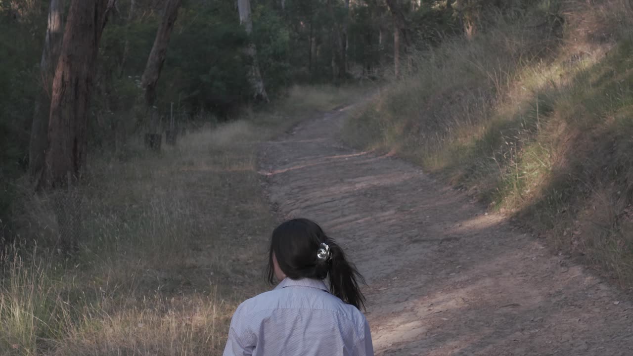 Girl walks a serene trail in Warrandyte Park as evening twilight casts a golden hue, picking up trash. Natural setting, engaging in environmental action amidst tranquil beauty