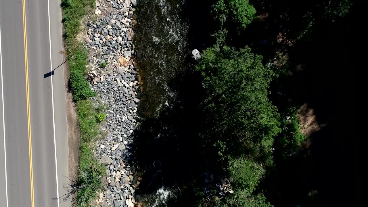 un río fluye pesado junto a una carretera mientras el dron desciende los autos pasan