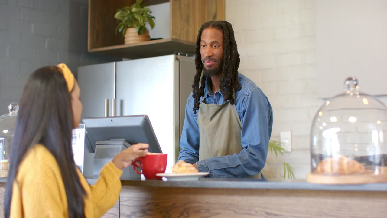 Barista hearing woman placing mug at counter serving pastry and confirming order in cafe