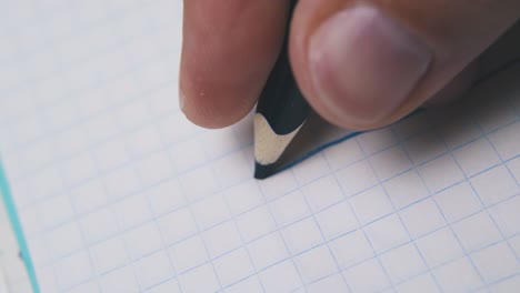 man draws line using dark blue pencil on checkered paper