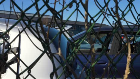 broken cars at car service seen through fence, pan right