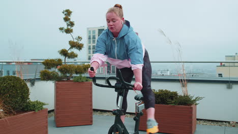 Mujer-Caucásica-Sana-Haciendo-Ejercicio-En-Una-Máquina-De-Ciclismo-Estacionaria-En-Bicicleta-En-El-Gimnasio-De-La-Azotea-De-La-Casa