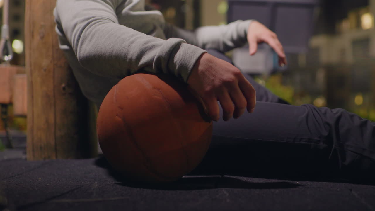 Mand på en bybænk om natten med en basketball, iført høretelefoner og beanie, lænet op ad en træstolpe under en gadelampe, byens skyline-bokeh, stille eftertænksom stemning, afslappet sweatshirt og sneakers