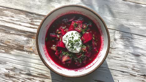 bowl of vibrant borscht with sour cream on rustic table