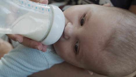 close up on a babyboy infant having his meal from the bottle with baby nutrition from mothers hands