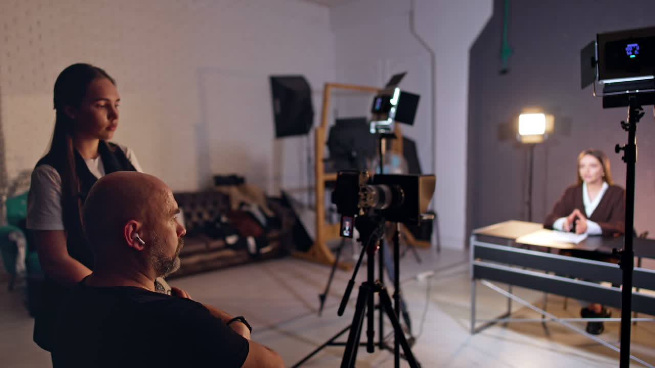 Man and young woman work at studio backstage. Cameraman and his assistant filming a female reporter in studio.