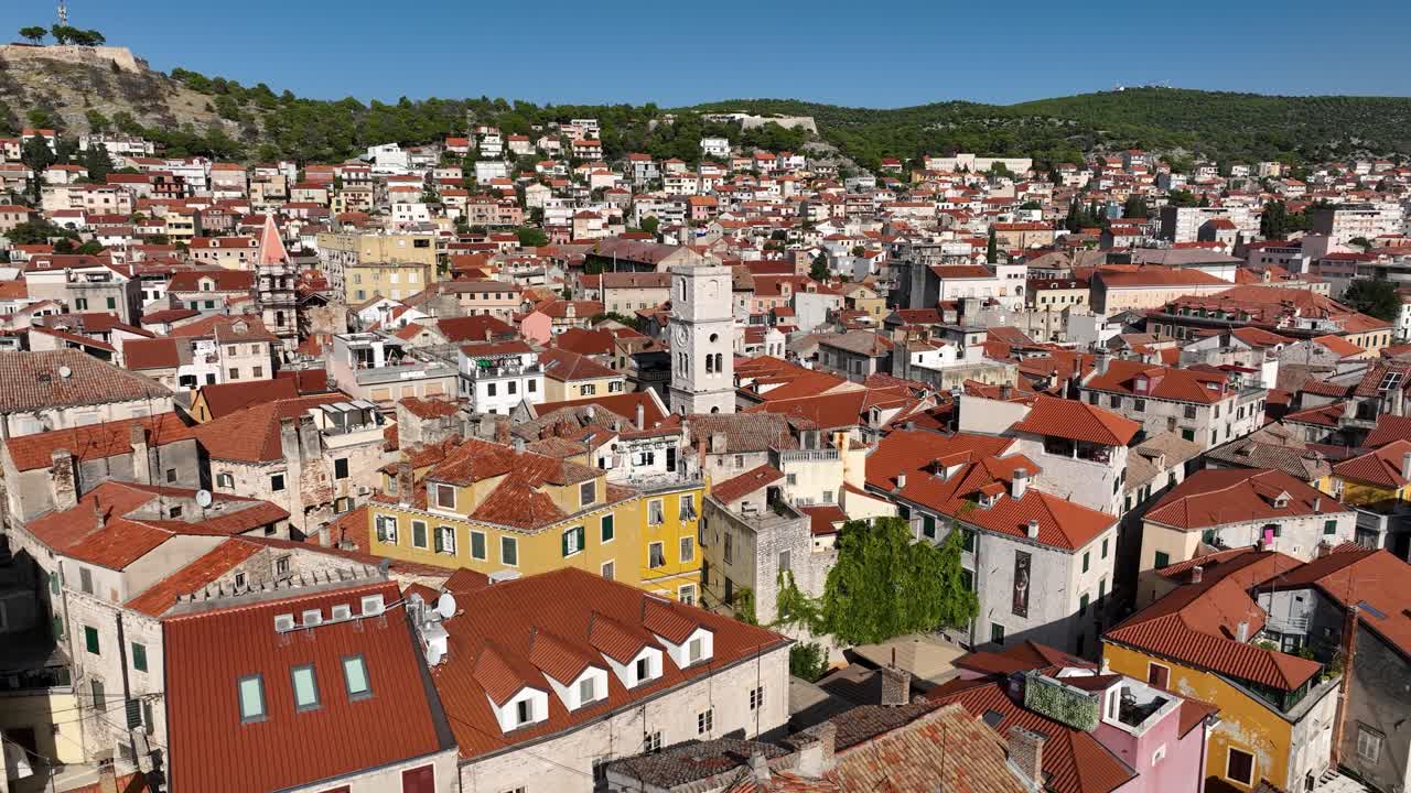 Aerial establishing orbit of Sibenik town with its charming red roofs and historic landmarks, set by the Adriatic Sea as boats docked along promenade bob in water
