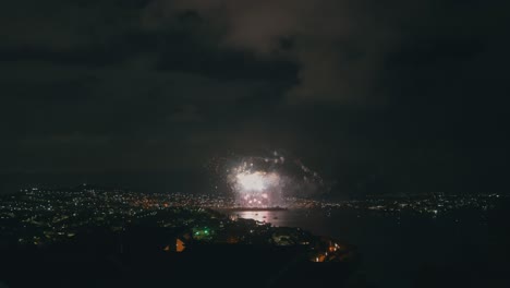 una toma captura la espectacular exhibición de fuegos artificiales que iluminan el cielo nocturno, vistos desde un punto de vista en la cima de una colina, brindando una vista panorámica de los colores vibrantes y de la pirotecnia