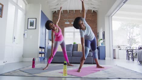 madre y hija afroamericanas felices haciendo yoga en la sala de estar, estirándose