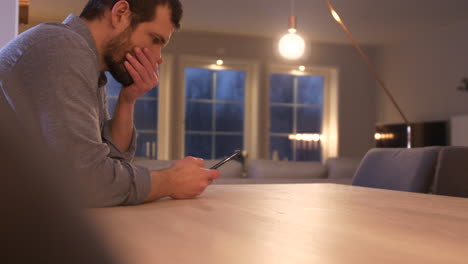 El-Hombre-Se-Sienta-En-La-Mesa-Leyendo-Un-Mensaje-De-Texto-Y-Empuja-Su-Teléfono-Con-Incredulidad