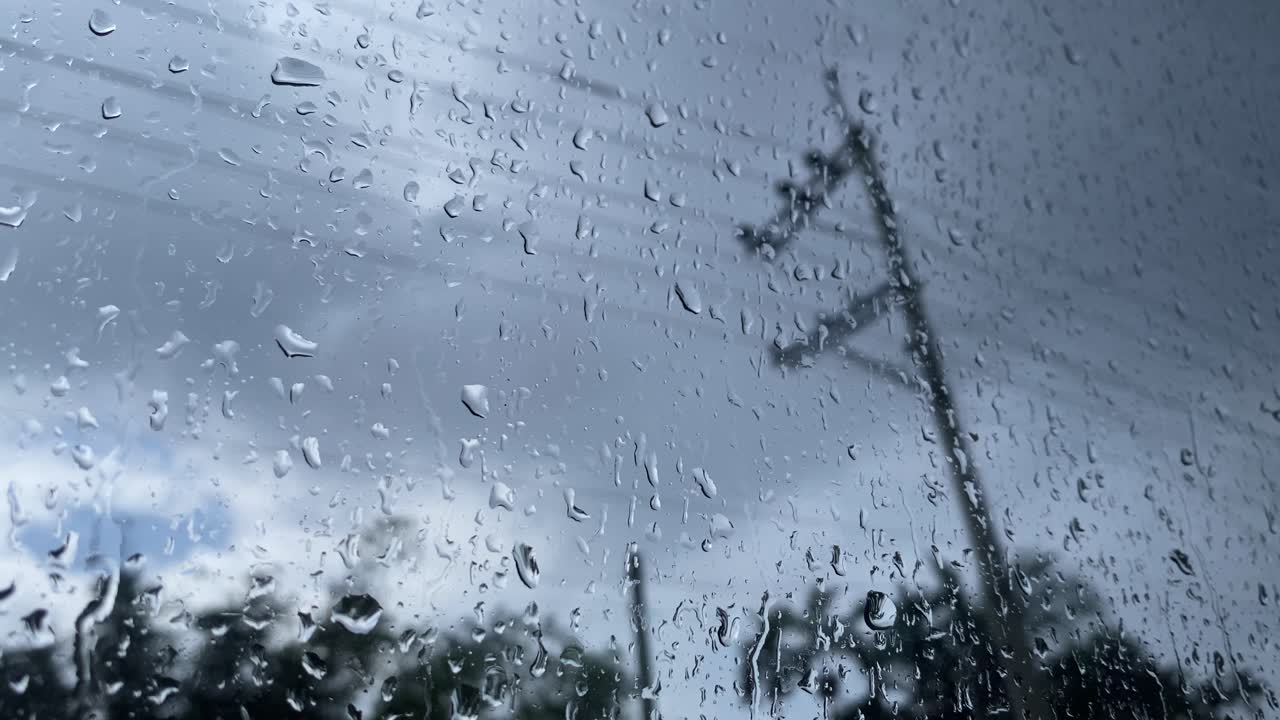 Close-up de gotas de água da chuva escorrendo na superfície da janela em um dia nublado e sombrio.