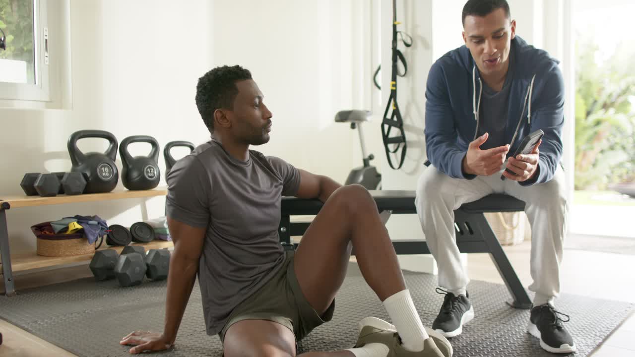 African American trainer pulling smartphone swiping app at gym while guiding client exercise