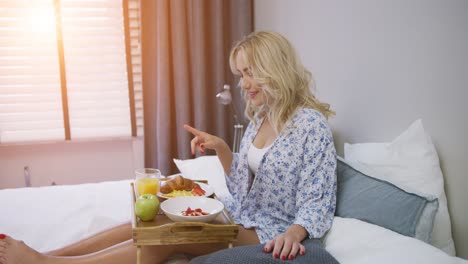 Una-Joven-Atractiva-Con-Camisa-Desayunando-Mientras-Está-Sentada-En-La-Cama-Con-Una-Bandeja