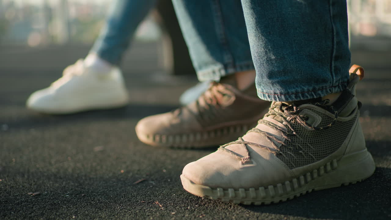 야외에 앉아있는 개인의 신발의 클로즈업, 하나는 갈색 운동화를 입고 다른 하나는 색 운동화를 착용하고, 자연 빛에서 텍스처 된 땅 표면에 고, 배경이 약간 흐릿합니다.