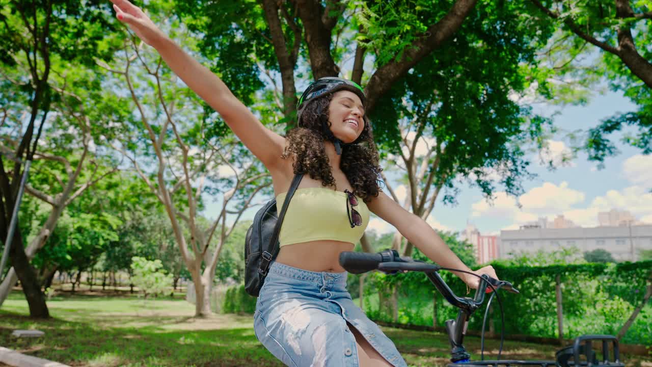 Happy young woman cycling in a park with outstretched arms