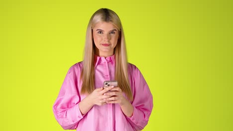 pretty blonde woman holding a smartphone, browsing scrolling the touch screen, colorful studio shot