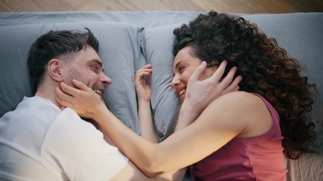 Casal feliz acariciando rostos, vista superior da cama. Homem e mulher se olhando ternamente pela manhã