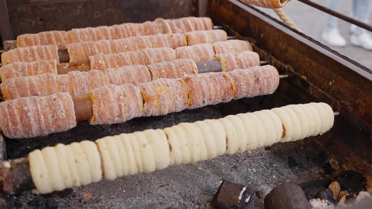Chimney cakes browning evenly on hot rollers with crisp crust forming in warm shop lighting