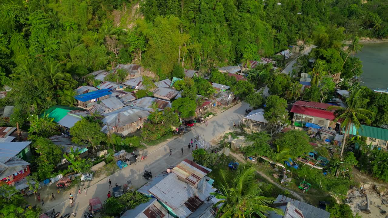Vila costeira pobre com crianças brincando na rua, cercada por casas simples e vegetação tropical exuberante. Bela vista aérea ascendente de drone panorâmico