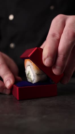 chef presenting a miniature sushi roll in a red box