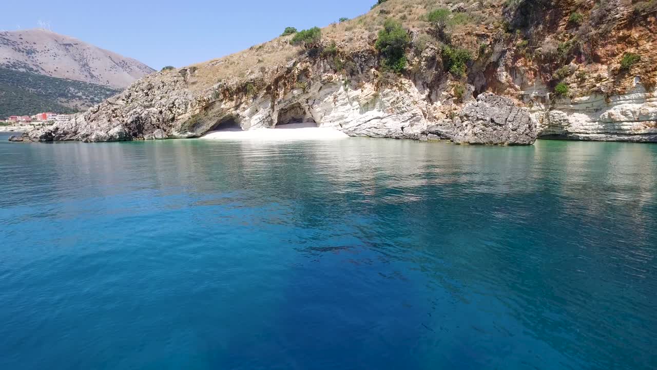 Approaching drone shot of a secret white sandy beach below an overhanging cliff in Kefalonia, located in the Ionian islands off the coast of Greece