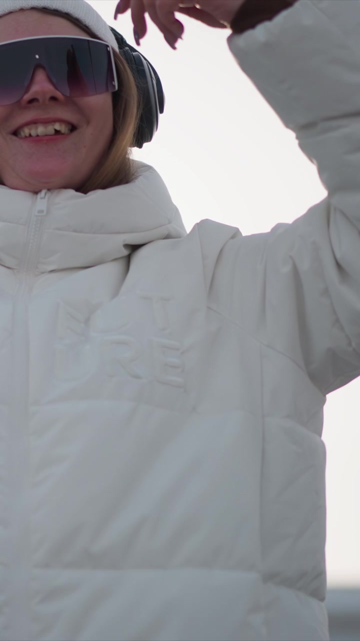 Woman wearing white puffer jacket black headphones and sunglasses gestures with her hands outdoors in cold weather. focuses on upper body and clothing details like texture or branding set