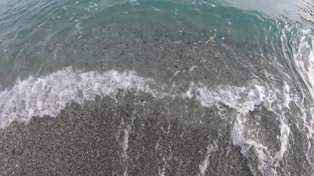 조약돌 해변에 서 있는 소녀의 다리는 바다 파도에 튀기고 지평선을 바라보고 있다