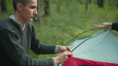 close up of person securing tent pole into camping fabric in forest setting as natural light filters through trees teamwork and preparation reflected in precise setup process for outdoor adventure