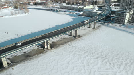 aerial, pan, drone shot, above pielisjoki, of cars, a bus and traffic on suvantosilta bridge, on a sunny, winter day, in joensuu, north karelia, finland