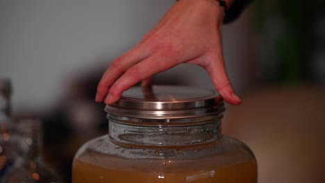 a stationary shot of a woman's hand while tightening the lid of a jar