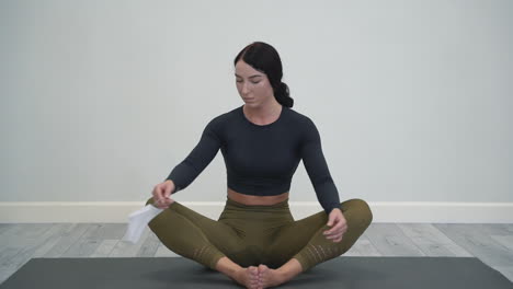 young woman doing yoga, meditating in lotus pose, puts on medical face mask. female athlete doing exercises indoors. white background and copy space.