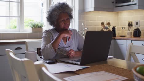 senior african american woman using laptop and calculating finances at home