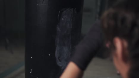 young woman training with a punching bag in a boxing club. back view of a young woman training with her hands wrapped in boxing