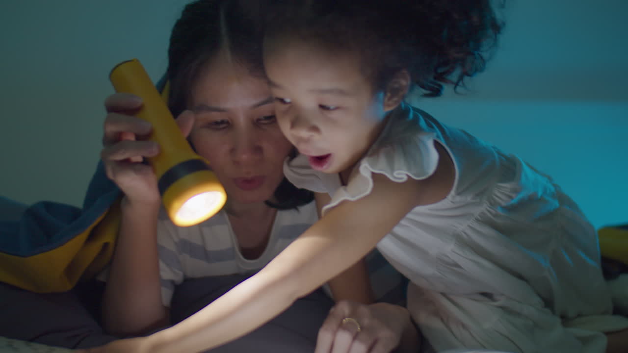 Asian Mother Reading Book to Little Daughter before Sleep