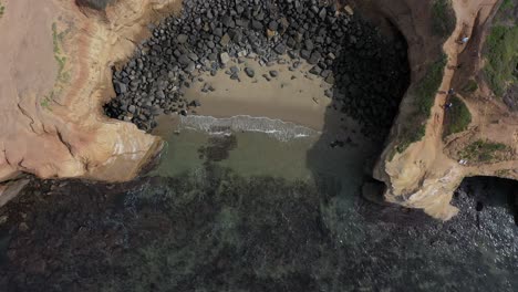 Aerial-drone-shot-captures-the-stunning-beauty-of-a-beach-surrounded-by-towering-cliffs-as-the-drone-slowly-ascends,-revealing-the-spectacular-coastline-scenery-from-above