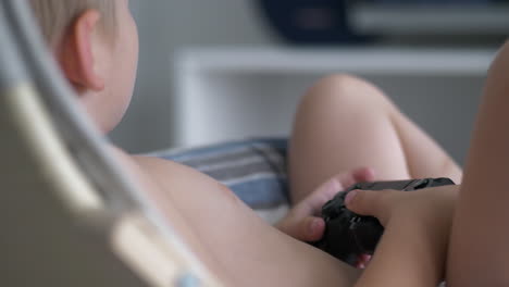 rear closeup of shirtless young boy child play games holding controller, indoor