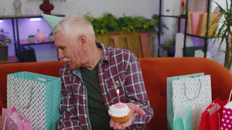 feliz anciano anciano abuelo hombre celebrando fiesta de cumpleaños, hace un deseo soplando vela ardiente