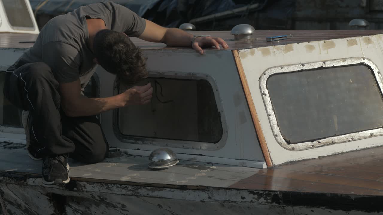 Young man removing sikaflex sealant flashing from aluminium windows Wooden boat